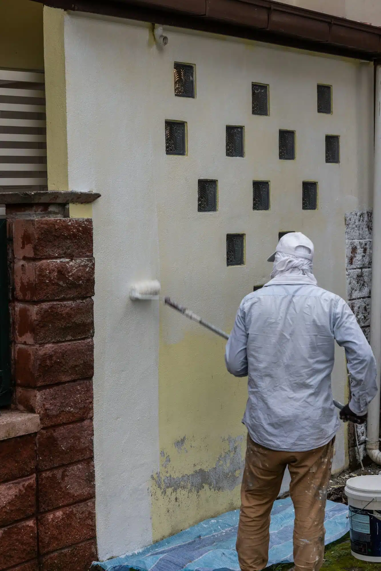 Painter worker adding undercoat foundation paint onto wall with roller at residential building in
